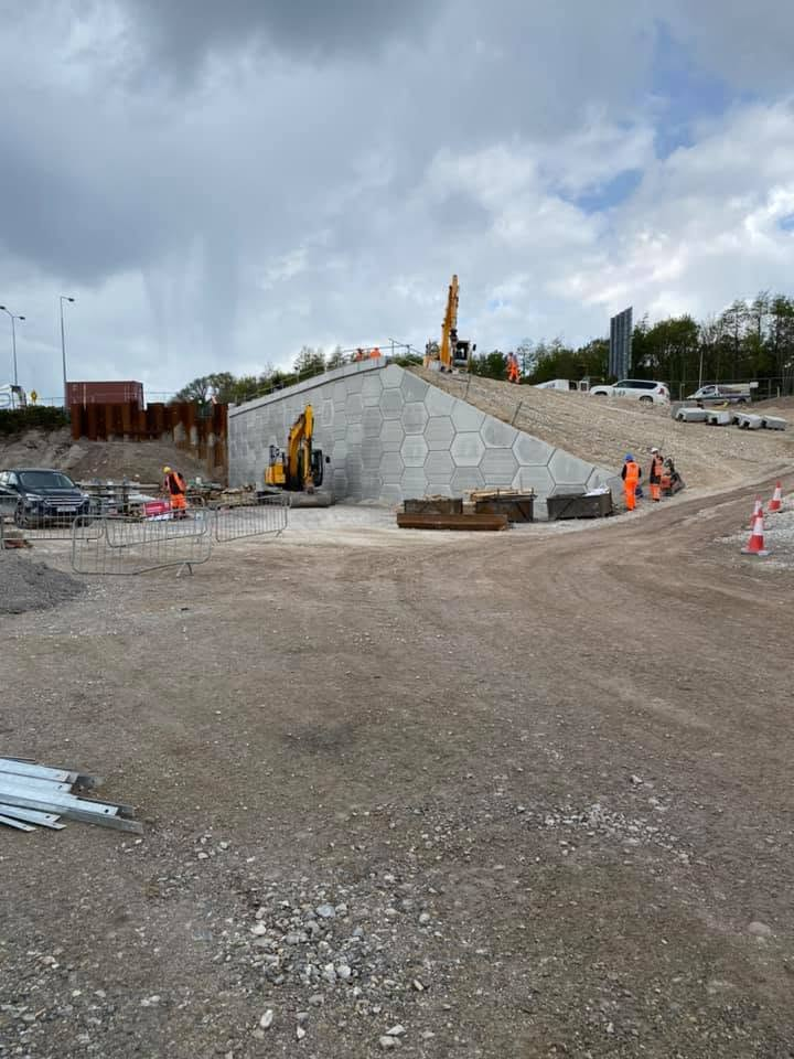 Bridge abutment with hexagonal facing and excavator on embankment
