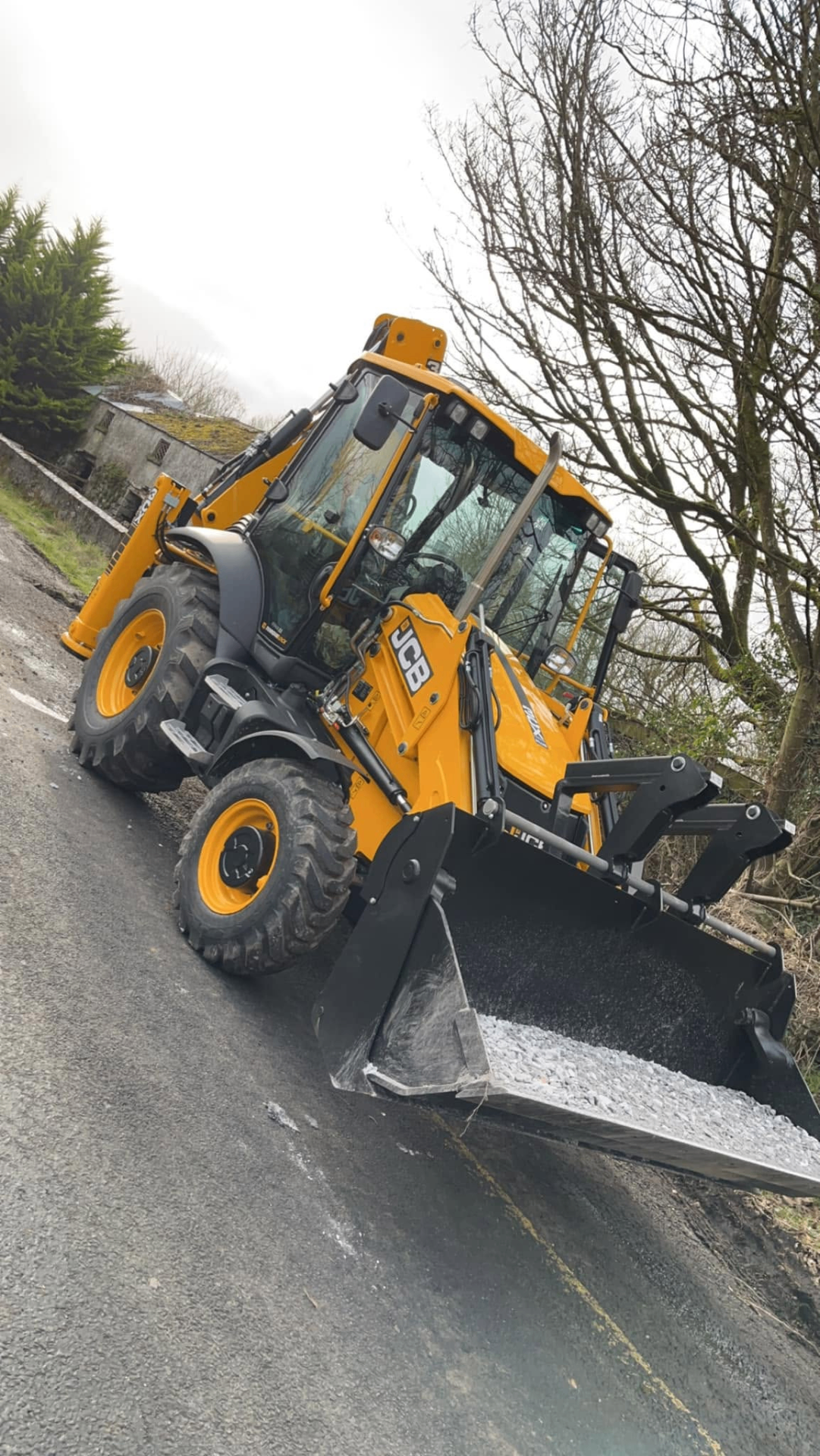 JCB 3CX backhoe loader on rural road with tarmac